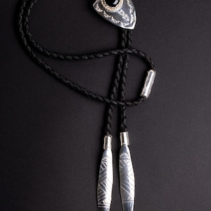 Puede incluir: Un corbatín de cuero negro con puntas de flecha plateadas y detalles de piedras preciosas negras.