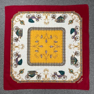 Può includere: Un fazzoletto quadrato rosso e bianco con un design dettagliato di carrozze. Il centro è giallo con un motivo decorativo. Il bordo presenta carrozze ornate in verde, viola e oro, con un bordo rosso.