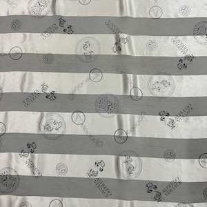 May include: A fabric with a repeating pattern of gray and white horizontal stripes. The design includes circular medallions, chain links, and the text "ALFREDO VERSACE" in a repeating pattern.