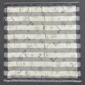 May include: A square silk scarf with a striped pattern in gray and white. The scarf features repeating circular medallions, chain links, and the text "ALFREDO VERSACE" along the borders. The scarf is a luxury fashion accessory.