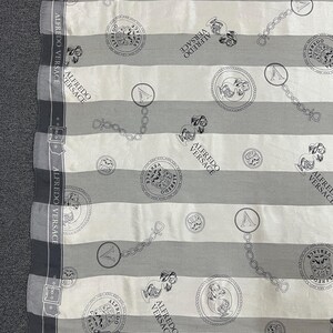 May include: A scarf with a striped pattern in white, light gray, and dark gray. The scarf features repeating circular medallions, chain links, and the text "ALFREDO VERSACE". The edges are bordered with a dark gray design.