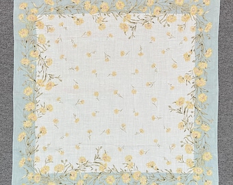 May include: A square, light blue handkerchief with a floral design. The border features yellow flowers and green stems. Scattered yellow flowers are also present on the white center. The words "Ralph Lauren" are printed in the bottom right corner.