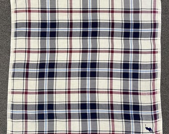 May include: Square white handkerchief with a plaid pattern in navy, burgundy, light blue, and gray. A small navy blue logo of a person on a horse is in the bottom right corner. The handkerchief is made of a soft fabric.