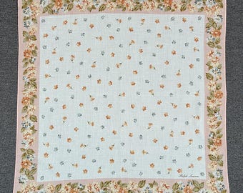 May include: Square, floral-patterned handkerchief with a light pink border. The center features small, scattered flowers in shades of orange, blue, and brown. The border is adorned with a floral design. The brand name "Ralph Lauren" is printed in the bottom right corner.