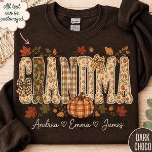 May include: A dark chocolate brown crewneck sweatshirt featuring the word GRANDMA in large, patterned letters with autumn-themed floral, plaid, and pumpkin prints. Below the text, the names Andrea, Emma, and James are printed in white.