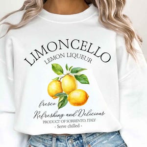 May include: White sweatshirt with a "Limoncello Lemon Liqueur" design. The graphic features three yellow lemons with green leaves, and the text "fresco, Refreshing and Delicious, Product of Sorrento, Italy - Serve chilled -."