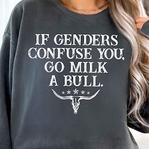 May include: Dark gray sweatshirt with the text "IF GENDERS CONFUSE YOU, GO MILK A BULL." in white, along with a bull skull graphic. The sweatshirt has a crew neck and long sleeves.