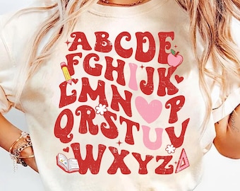 May include: A white t-shirt with a red alphabet design. The letters are in a retro style and are surrounded by small illustrations, including a pencil, a heart, a flower, an apple, a book, and a triangle. The text on the shirt reads "ABCDEFGHIJKLMNOPQRSTUVWXYZ".