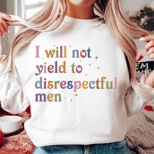 Puede incluir: Sudadera blanca con la frase "I will not yield to disrespectful men" en letras coloridas de estilo retro. El diseño incluye pequeños acentos de estrellas. Una prenda casual y con mensaje.