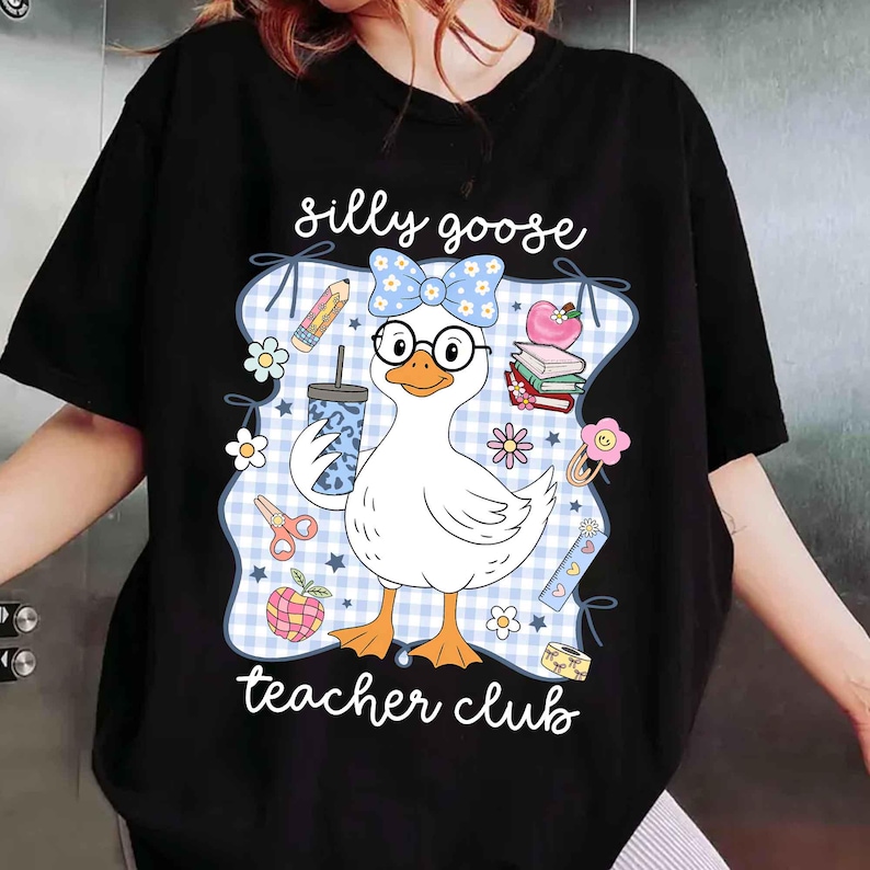 K&ouml;nnte beinhalten: Schwarzes T-Shirt mit einer Cartoon-Gans, die eine Brille und eine Schleife tr&auml;gt und ein Getr&auml;nk h&auml;lt. Das Design enth&auml;lt den Text "silly goose teacher club" mit Illustrationen zum Thema Schule.
