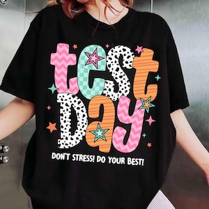 May include: Black t-shirt with a colorful graphic that says "test day" with stars and the text "Don't stress! Do your best!"