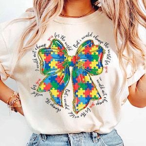 May include: A white t-shirt with a colorful puzzle piece bow and the text "I would not change the world for you. But I would change the world for you."