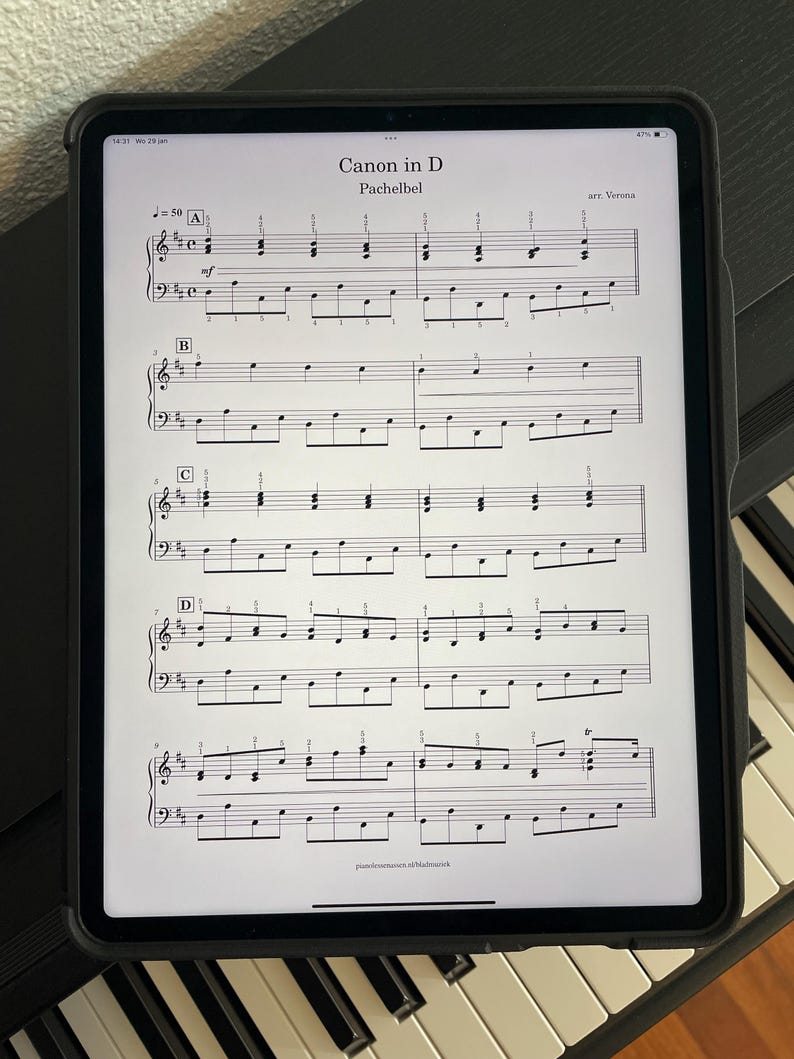 May include: A digital tablet displaying sheet music for Pachelbel's Canon in D, resting on a piano. The music is in black and white, with the title and composer's name visible at the top. The tablet is in a black case.
