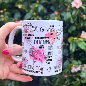 May include: White ceramic mug with a handle, featuring floral and inspirational text in black and pink. The mug includes phrases like "I am worthy AF" and "Celebrate every damn win."