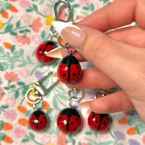 May include: A collection of four ladybird keychains, each featuring a glossy red body with black spots and a black head. Each ladybird is attached to a silver-toned metal lobster clasp by a small circular jump ring, creating a functional accessory.