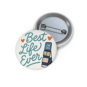 Puede incluir: Una chapa redonda con alfiler que presenta un fondo blanco, el texto Best Life Ever en cursiva de color azul cerceta, dos pequeños corazones naranjas y un expositor de literatura azul oscuro con el texto JW.ORG. El reverso muestra un alfiler.