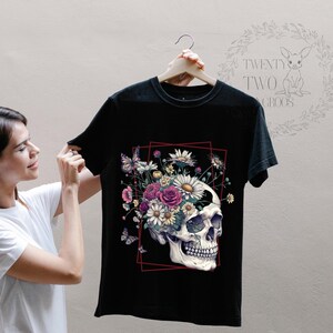 Peut inclure: T-shirt noir avec un motif de cr&acirc;ne sur lequel poussent des fleurs. Le cr&acirc;ne est blanc et les fleurs sont roses, blanches et jaunes. Le texte "TWENTY TWO CROCS" est sur le dos du t-shirt.
