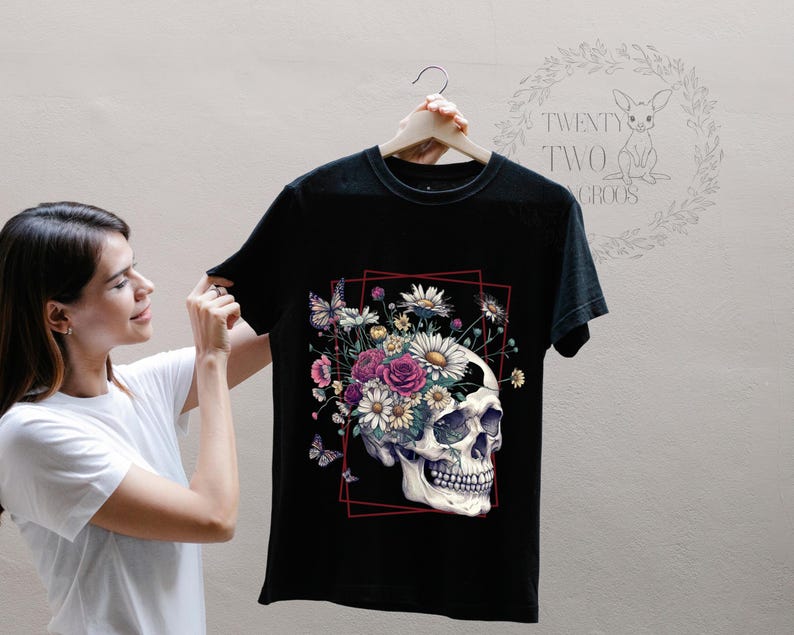 Peut inclure: T-shirt noir avec un motif de cr&acirc;ne sur lequel poussent des fleurs. Le cr&acirc;ne est blanc et les fleurs sont roses, blanches et jaunes. Le texte "TWENTY TWO CROCS" est sur le dos du t-shirt.