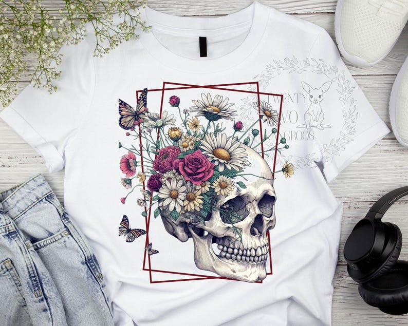 Peut inclure: T-shirt blanc avec un motif de cr&acirc;ne orn&eacute; de fleurs et de papillons. Le cr&acirc;ne est entour&eacute; d'un cadre rouge.