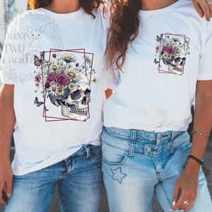 Peut inclure: Deux t-shirts blancs avec un motif de cr&acirc;ne. Le cr&acirc;ne est entour&eacute; de fleurs et de papillons. Le texte "TWENTY TWO KANGAROOS" est sur le t-shirt de gauche.