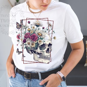 Peut inclure: T-shirt blanc avec un motif de cr&acirc;ne sur lequel poussent des fleurs. Les fleurs sont roses, blanches et jaunes.