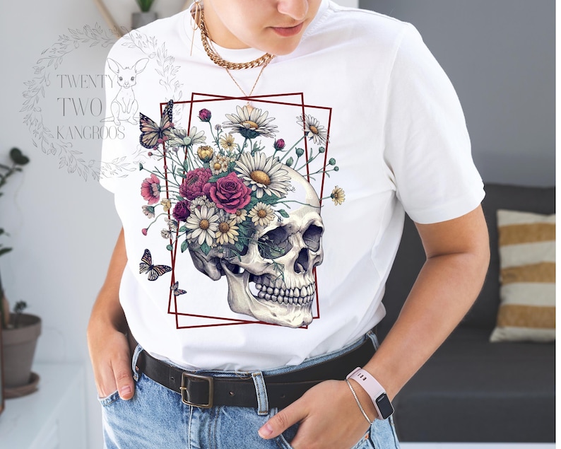 Peut inclure: T-shirt blanc avec un motif de cr&acirc;ne sur lequel poussent des fleurs. Les fleurs sont roses, blanches et jaunes.