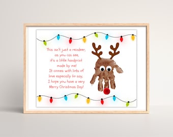 May include: A framed Christmas print featuring a handprint reindeer with googly eyes and brown antlers. The reindeer has a red nose. The print includes the text "This isn't just a reindeer...Merry Christmas Day!" and is decorated with colorful string lights.