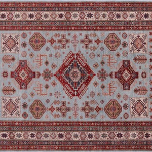 May include: Rectangular area rug with a light blue field and a detailed border. The rug features a central diamond design in red and navy, surrounded by geometric patterns in red, brown, and beige. The border is a deep red with repeating star motifs.