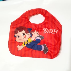 May include: Red tote bag with a cartoon illustration of a girl in a yellow shirt and blue overalls. The bag has a handle and the word "Peko" in white. The bag has vertical red stripes.