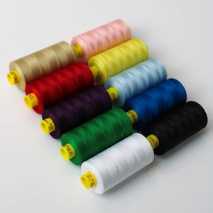 May include: A collection of spools of thread in various colors, including beige, red, purple, green, white, black, blue, yellow, and pink. Each spool has a yellow base.
