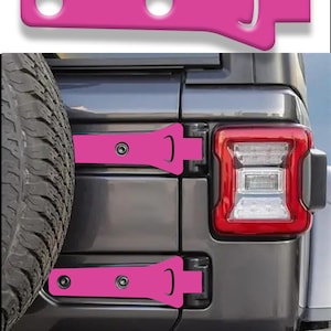 May include: A set of two bright pink hinge covers designed for a vehicle tailgate. Each cover features a flat, elongated shape with two circular holes for mounting hardware and a curved cutout on the right side, shown installed on a dark gray SUV.
