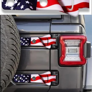 May include: Two rectangular hinge covers for a vehicle, featuring a printed American flag design with white stars on a blue field and red and white stripes. Each cover has two circular cutouts and a curved end, shown installed on a dark gray vehicle.