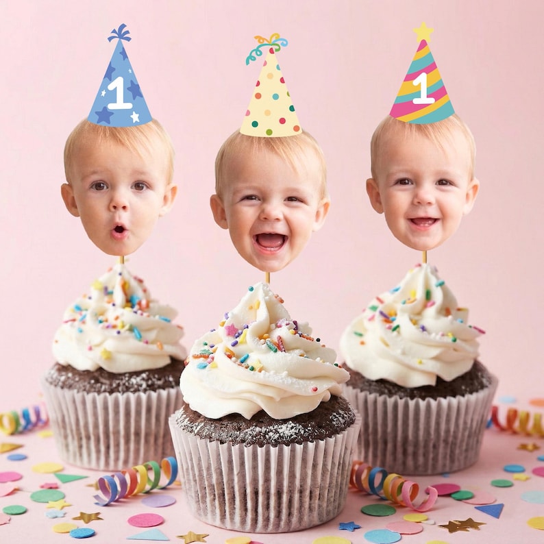 May include: Three chocolate cupcakes with white frosting and colorful sprinkles. Each cupcake has a photo of a baby's face attached to a stick, wearing a party hat with the number 1. Confetti and streamers are scattered around.