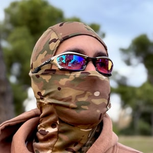 Puede incluir: Una persona con un pasamontañas de camuflaje y una sudadera con capucha marrón. La persona también lleva gafas de sol con montura plateada y lentes reflectantes. El pasamontañas cubre la cabeza y el cuello, con un patrón de camuflaje.