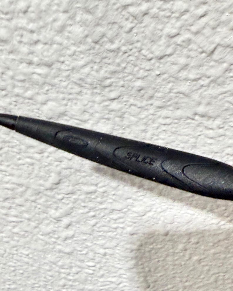 K&ouml;nnte beinhalten: Nahaufnahme eines schwarzen Objekts mit dem Aufdruck "SPLICE". Das Objekt hat eine ovale Form und eine strukturierte Oberfl&auml;che. Der Hintergrund ist eine wei&szlig;e, strukturierte Wand.