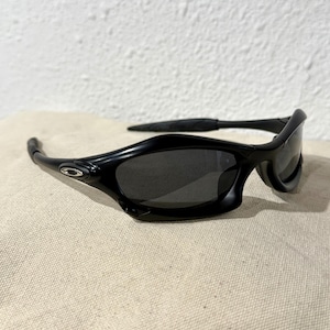 K&ouml;nnte beinhalten: Schwarze Sonnenbrille mit geschwungenem Rahmen und dunklen Gl&auml;sern. Die Sonnenbrille hat ein schlankes, modernes Design mit einem kleinen silbernen Logo an der Seite. Die B&uuml;gel umschlie&szlig;en die Ohren f&uuml;r einen sicheren Sitz.