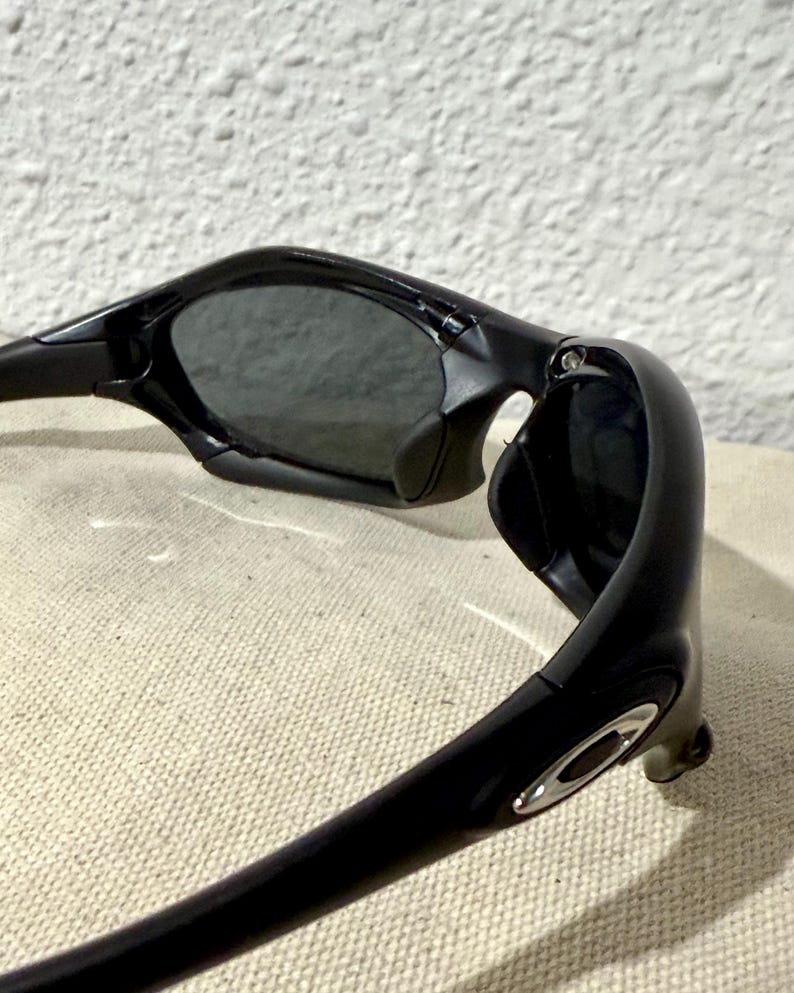K&ouml;nnte beinhalten: Schwarze Sonnenbrille mit einem schlanken, modernen Design. Die Sonnenbrille hat dunkle Gl&auml;ser und einen gl&auml;nzend schwarzen Rahmen. Der Rahmen hat einen silbernen Akzent in der N&auml;he des B&uuml;gels. Die Sonnenbrille ist abgewinkelt und zeigt Form und Stil.