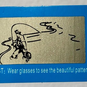 May include: A blue rectangular card with a silver rectangle in the center. The silver rectangle has a black illustration of a person fishing. The text at the bottom says, "TEST: Wear glasses to see the beautiful pattern."
