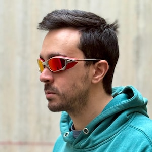 Puede incluir: Gafas de sol tintadas en rojo y amarillo con montura plateada y protectores laterales rojos. La persona lleva una sudadera con capucha turquesa.