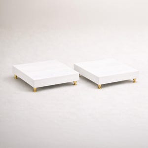 May include: A white ceramic mug with a black handle and the text "But First, Coffee" in a bold, black font. The mug is set against a blurred background, suggesting a cozy setting.