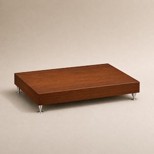 May include: A rectangular wooden display riser with a smooth, dark brown finish. The platform is elevated by four small, metallic, cone-shaped feet positioned at each corner, providing a stable base for the flat, solid wood surface.