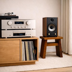 May include: A stereo system with a silver receiver and CD player on a wooden cabinet. A wooden speaker with a black front sits on a small wooden stool. Vinyl records are stored in the cabinet below the stereo components.