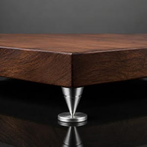 Puede incluir: Una losa rectangular gruesa de madera marrón oscuro con un patrón de veta natural visible, sostenida por un solo pie de metal cónico de color plateado pulido con una base circular plana, posicionado en la esquina de la plataforma de madera.