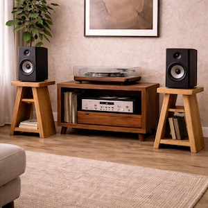 May include: A home entertainment setup featuring two black speakers on wooden stands, a wooden media console with a turntable, and a silver stereo receiver. The room has a neutral color palette.