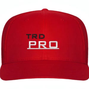 May include: A red baseball cap with a mesh back. The front of the cap features the embroidered text "TRD PRO" in black and white. The cap has a curved brim and a structured crown.