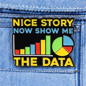 May include: A black and yellow enamel pin with the text "Nice story now show me the data" and a bar graph and pie chart.