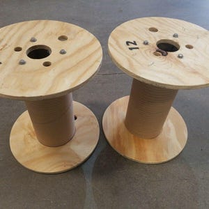 May include: Two wooden spools with a hole in the center and the number "12" written on the top. The spools are made of light brown wood and have a natural finish.