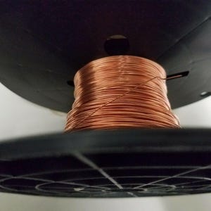 May include: A spool of copper wire wound around a black plastic base. The wire is a shiny, reddish-brown color.