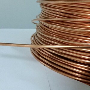 May include: A spool of copper wire, with a single strand extending outward. The wire has a shiny, reddish-brown color and is tightly wound. The image is a close-up, highlighting the texture and color of the metal.