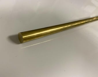 May include: A solid, cylindrical metal rod with a polished, reflective gold-colored finish. The rod features a smooth, uniform surface and a circular cross-section, extending diagonally across the frame from the lower left to the upper right.